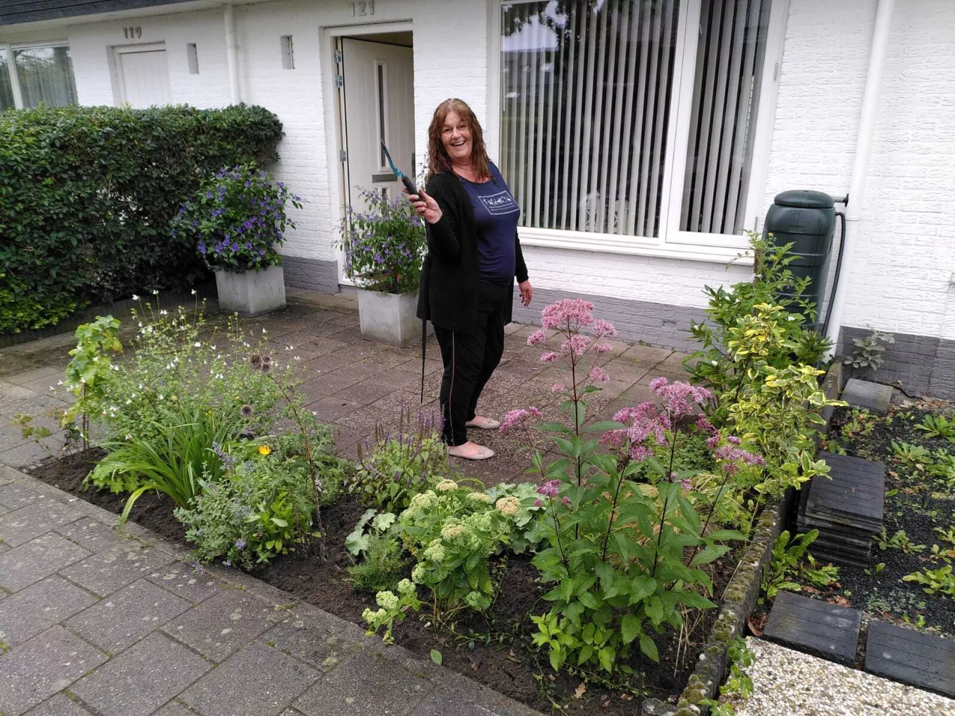 Huurder staat in voortuin en houdt tuingereedschap in de lucht
